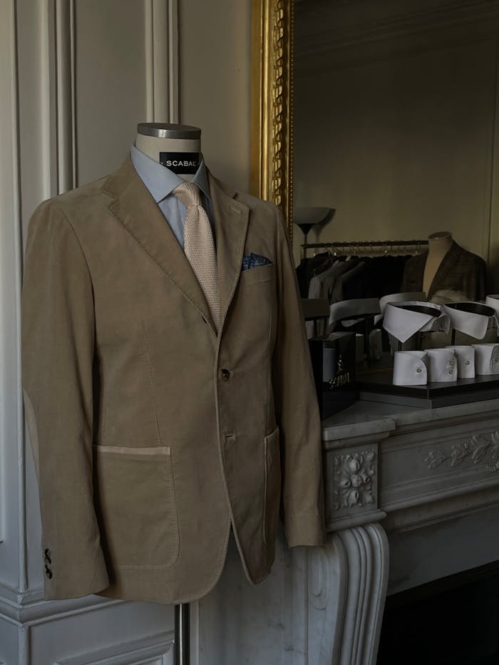 gallery-4 Stylish beige suit displayed on a mannequin in a tailor's shop with classic decor.