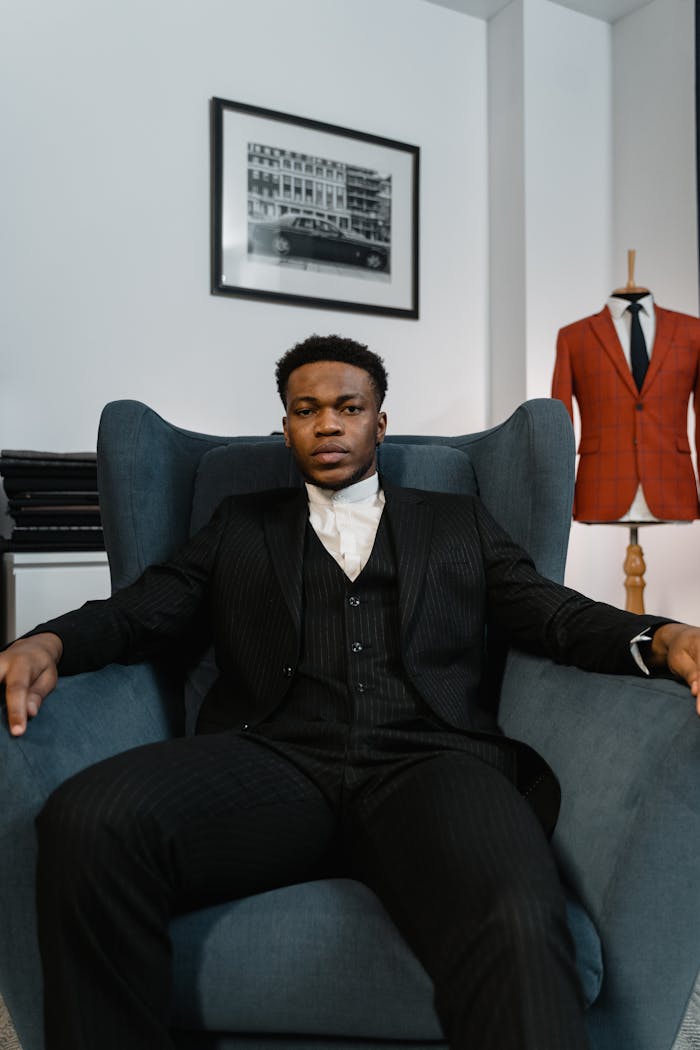 why-choose-us Elegant businessman in a black suit sitting confidently in a modern interior, exuding sophistication and style.