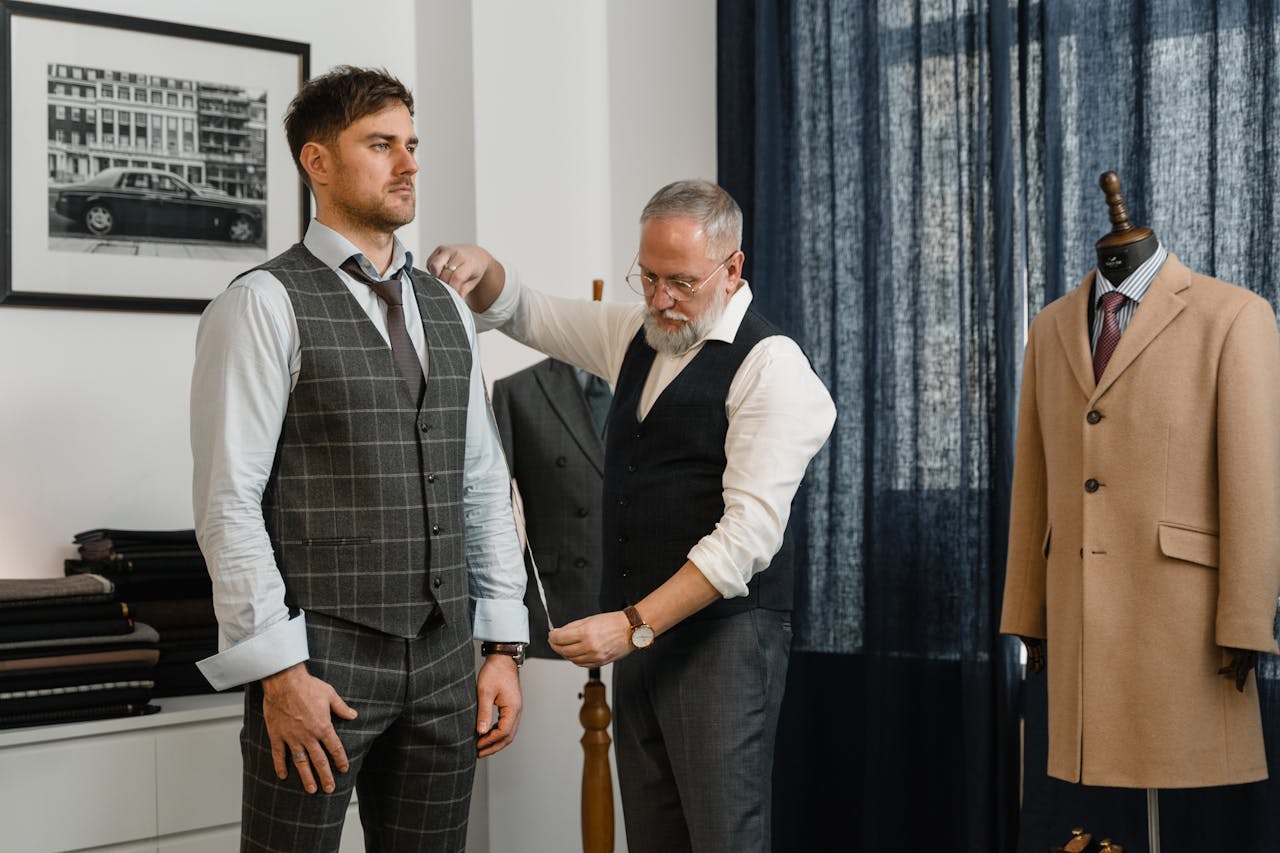 hero-img-01 Tailor adjusts a client's suit in a classic atelier setting, emphasizing craftsmanship.